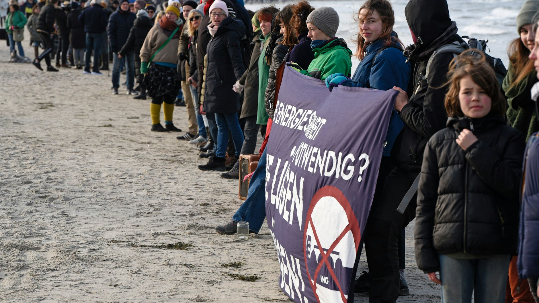Mit einem Transparent mit der Aufschrift "Für die Energiesicherheit notwendig? Keine Lügen vor Rügen" stehen Menschen am Strand von Binz auf der Insel Rügen in einer Menschenkette als Protest gegen ein vor der Insel vorgesehenes Flüssigerdgas-Terminal. 