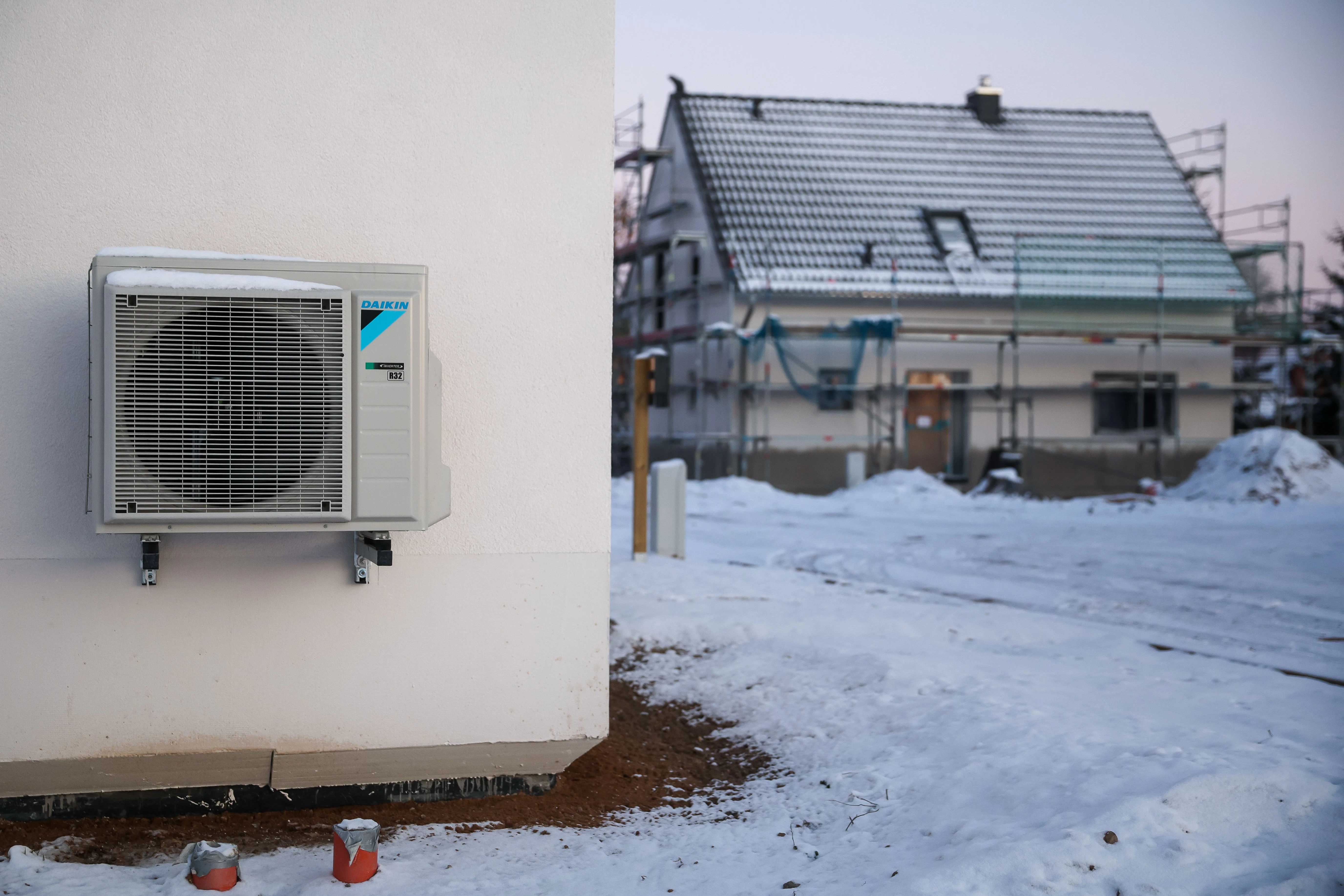 Sachsen, Leipzig: Eine Luftwärmepumpe hängt bei Schnee und Eis an einer Hauswand in einem neu entstehenden Einfamilienhausgebiet. Luft-Wärmepumpen gelten als die günstigeren Alternativen zu Gasheizungen, verbrauchen im Winter allerdings mehr Strom.