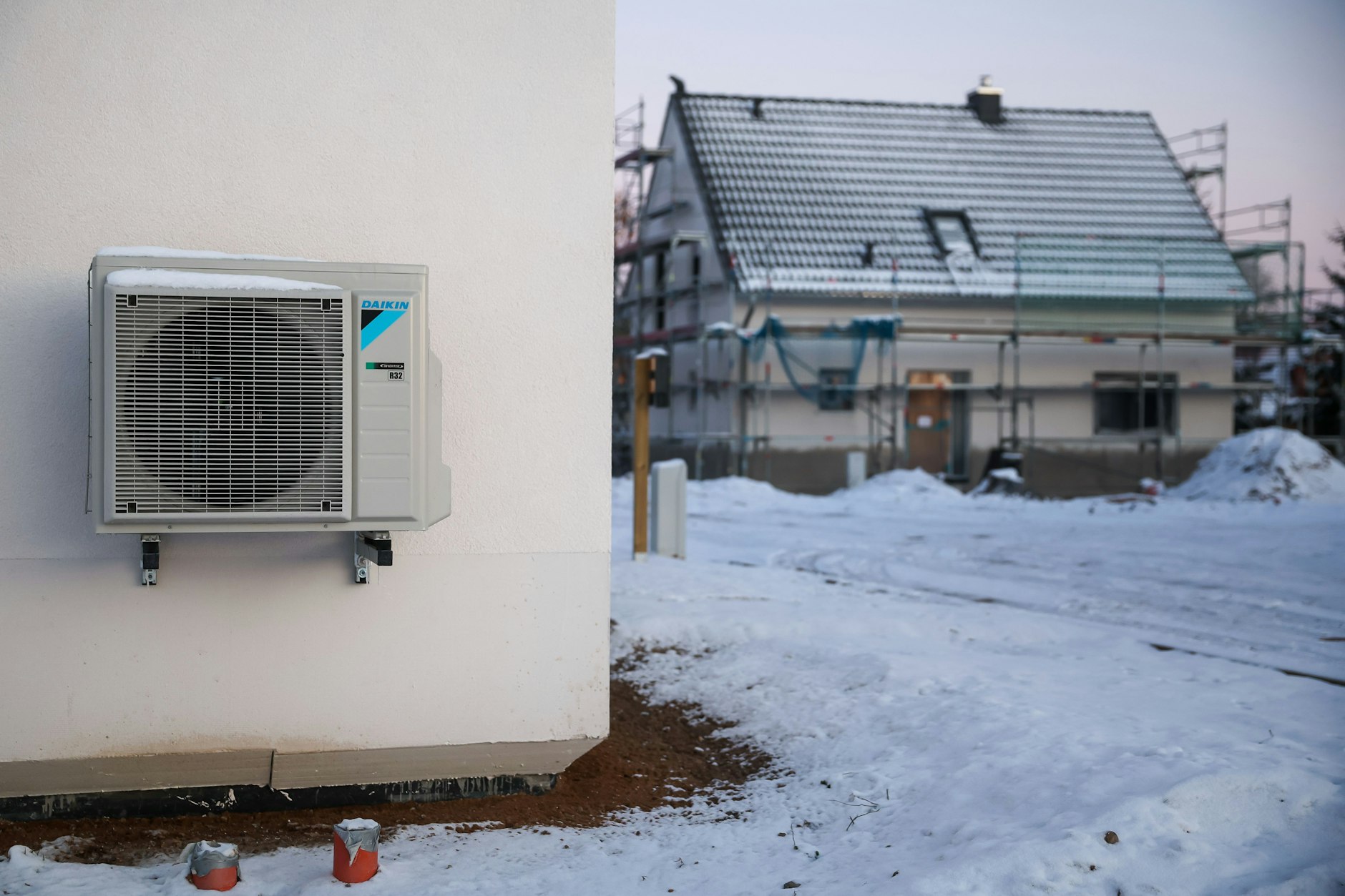 Sachsen, Leipzig: Eine Luftwärmepumpe hängt bei Schnee und Eis an einer Hauswand in einem neu entstehenden Einfamilienhausgebiet. Luft-Wärmepumpen gelten als die günstigeren Alternativen zu Gasheizungen, verbrauchen im Winter allerdings mehr Strom.