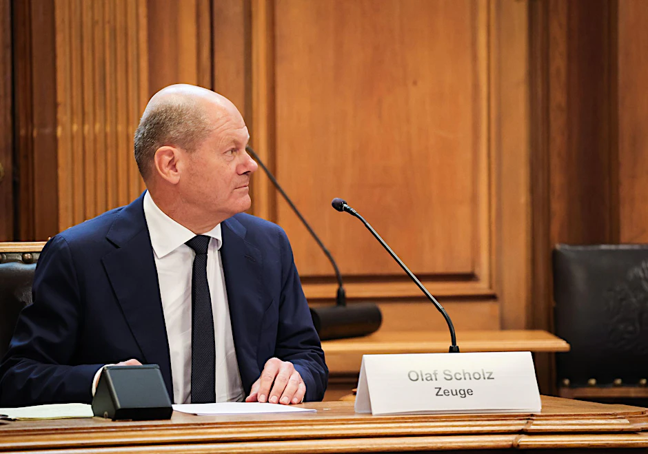 Bundeskanzler Olaf Scholz (SPD) auf der Senatsbank mit einem Plastikschild mit dem Text „Olaf Scholz Zeuge“.