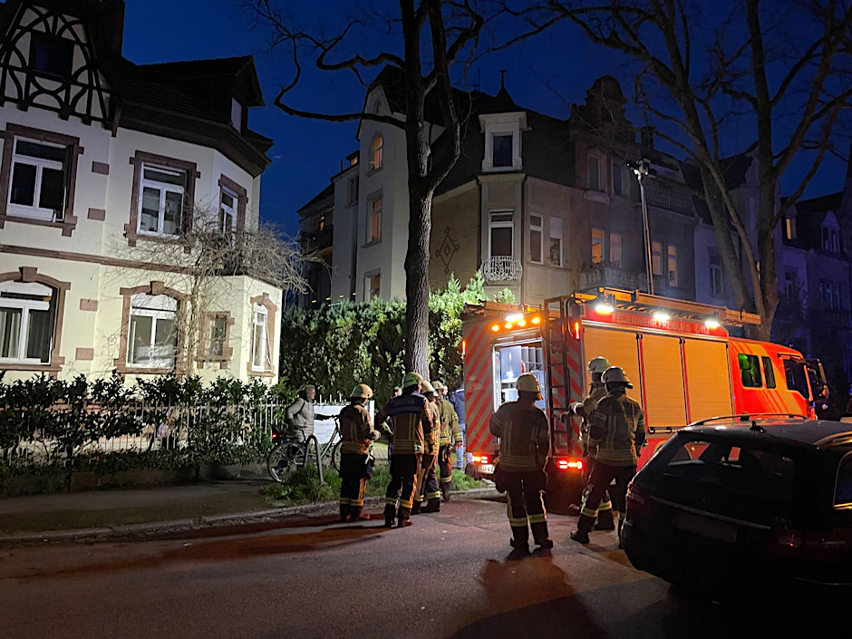 Einsatzkräfte der Feuerwehr stehen an dem Wohnhaus, in dessen Untergeschoss sich eine Explosion ereignete.  