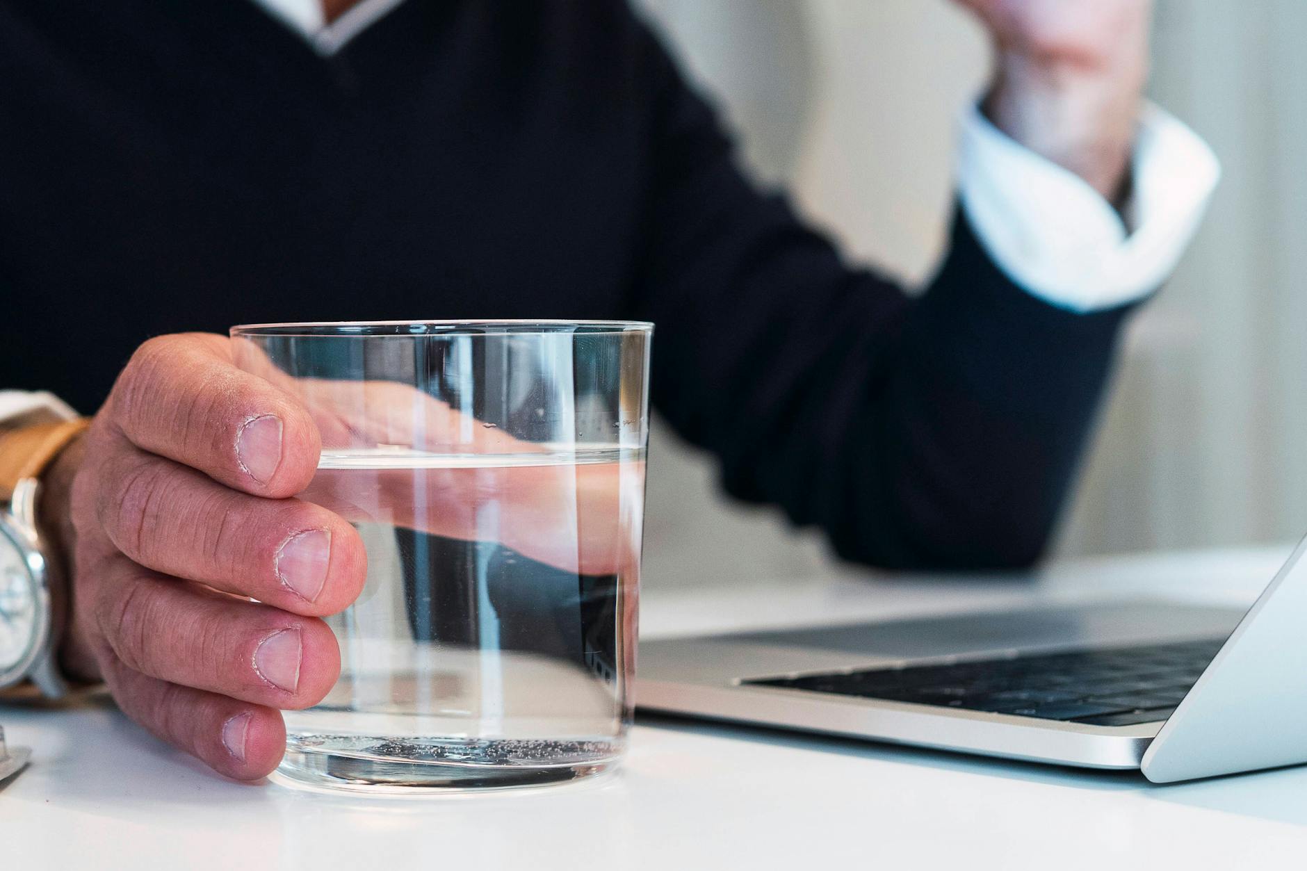 Eine Person mit einem Glas Wasser an einem Laptop