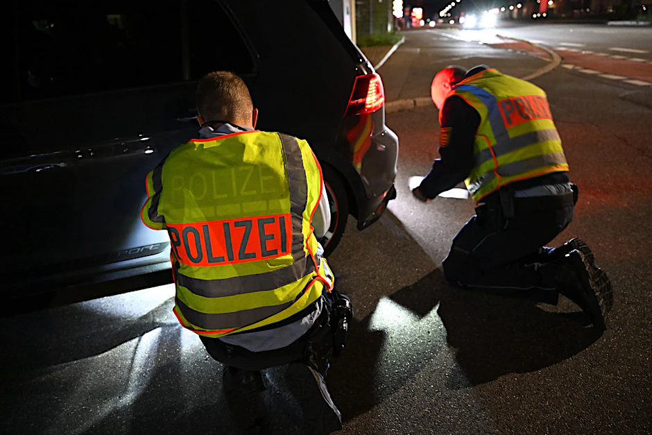 Polizisten suchen im Radkasten und am Heck eines Autos nach verdächtigen Gegenständen (Symbolbild).&nbsp;