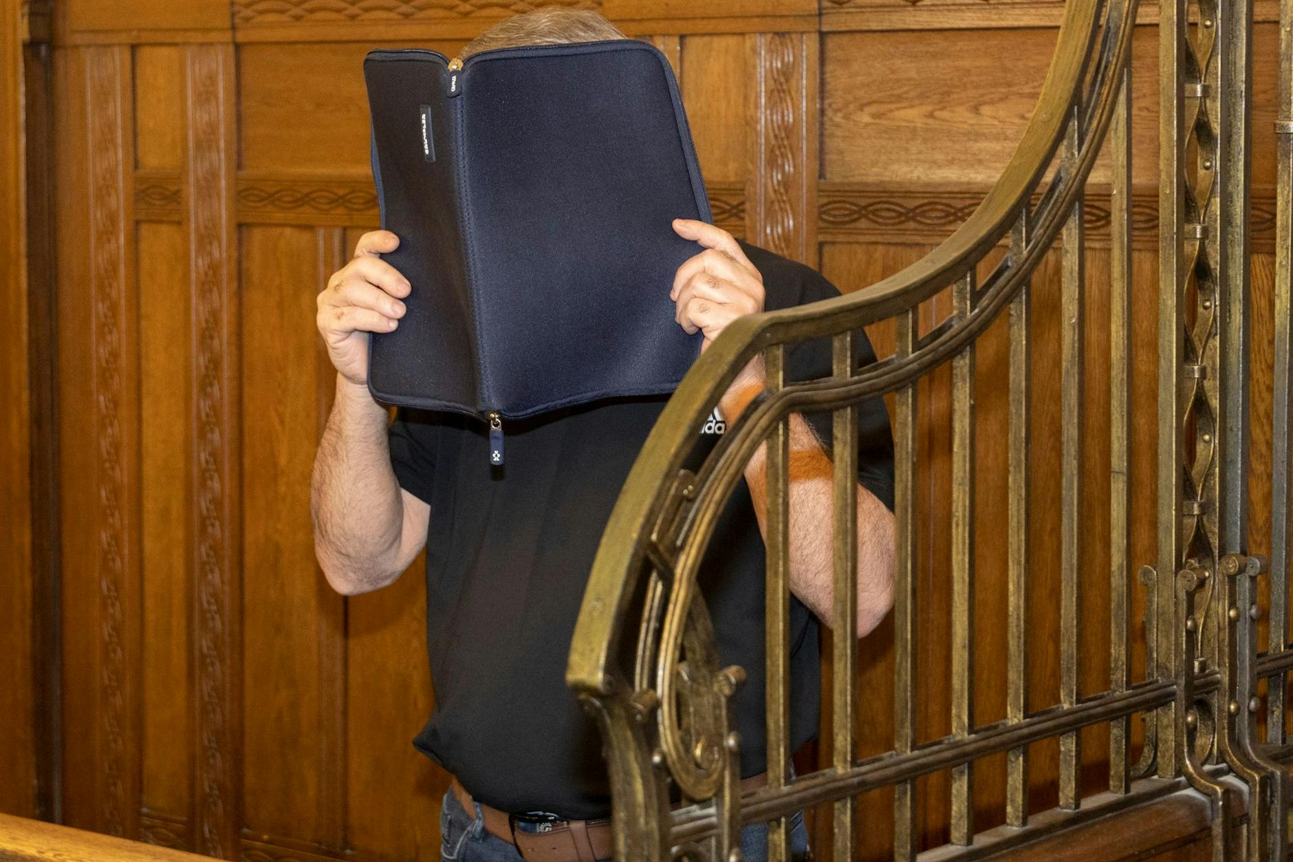 Der 51-jährige Angeklagte versteckt sein Gesicht hinter einer Aktentasche. 