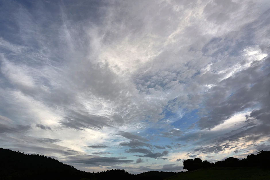Eine aufreißende Wolkendecke zieht über eine Wiese hinweg.  