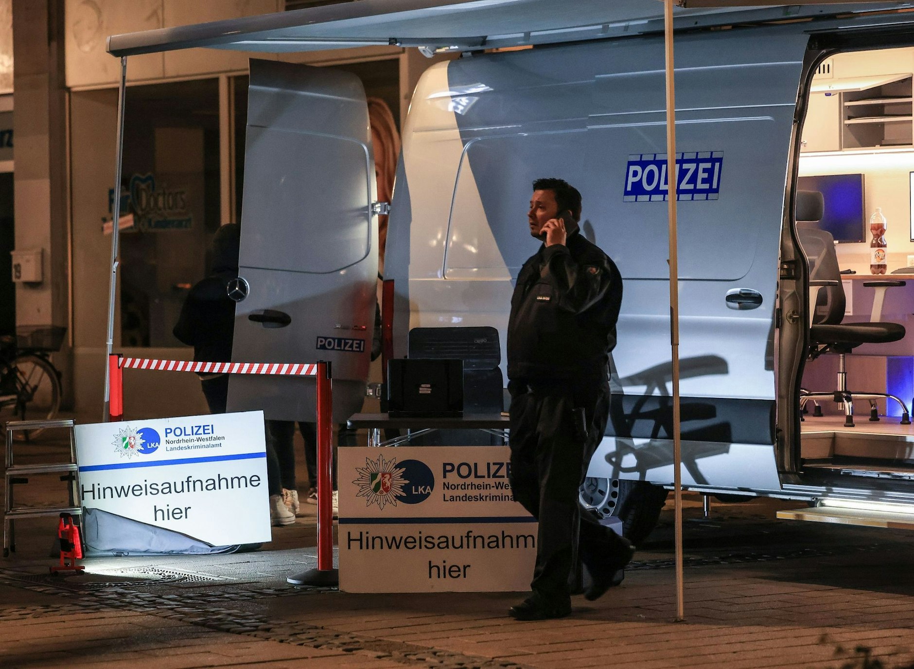 Ein Polizist steht in der Nähe des Tatortes vor einem Einsatzfahrzeug.  