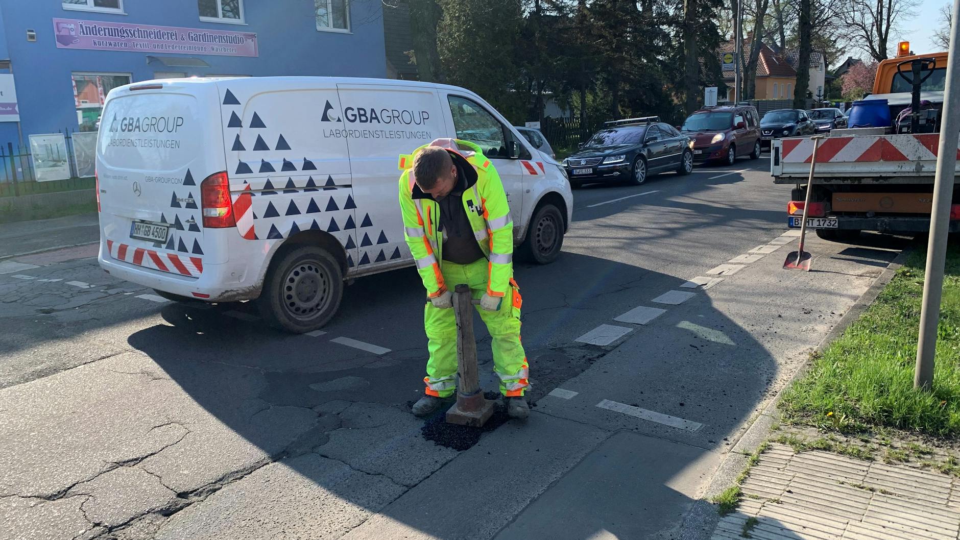 Ein Straßenbauer stampft den Kaltasphalt fest, den er in ein Schlagloch der rissigen Straße geschippt hat. Die Köpenicker Straße muss er oft zwecks „Gefahrenabwehr“ aufsuchen.