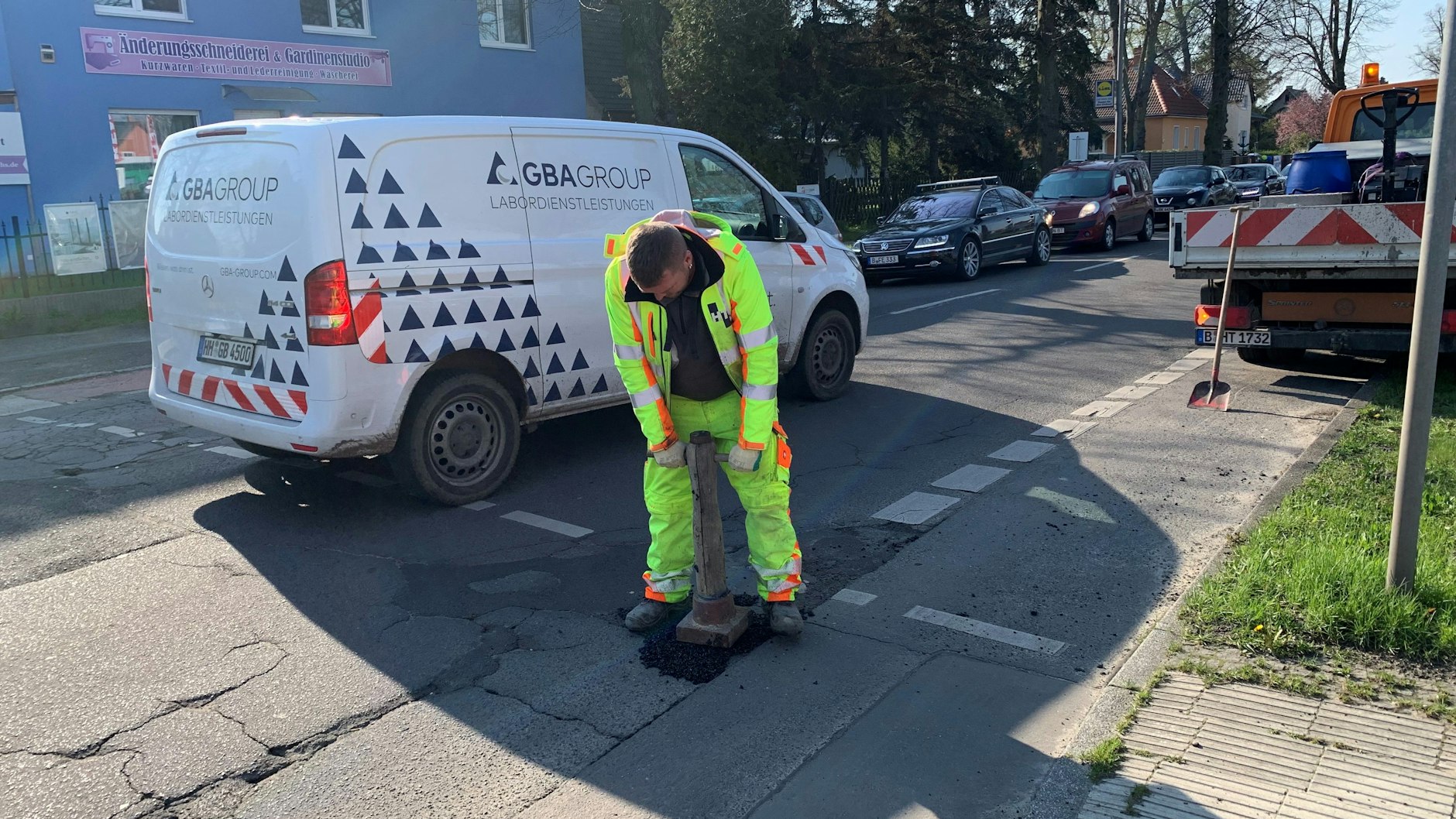 Ein Straßenbauer stampft den Kaltasphalt fest, den er in ein Schlagloch der rissigen Straße geschippt hat. Die Köpenicker Straße muss er oft zwecks „Gefahrenabwehr“ aufsuchen.