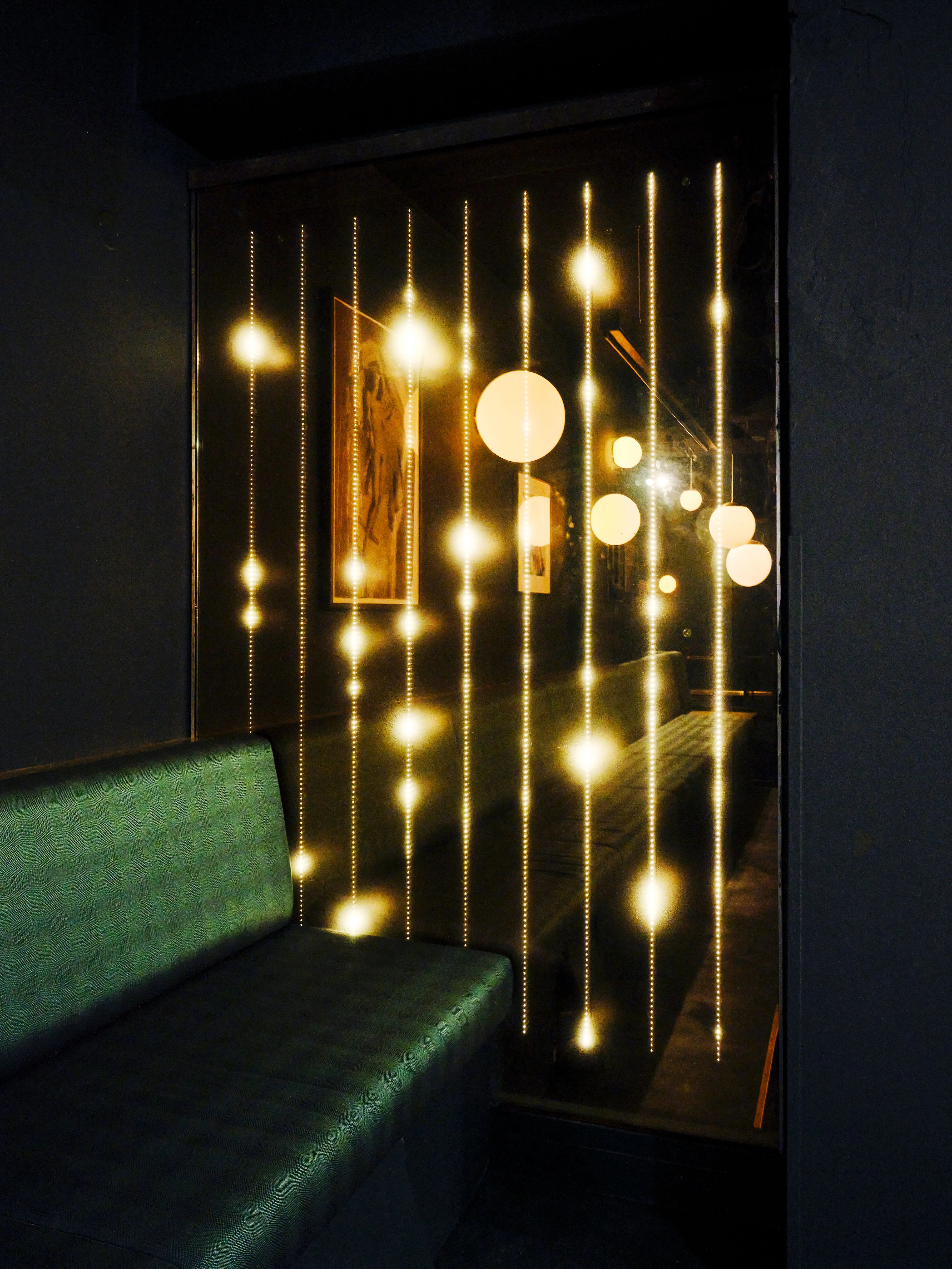 LED-Goldregen, der an den alten Fensterscheiben des Palasts der Republik hinabläuft. Im Glas spiegeln sich die in „British Racing Green“ bezogenen Bänke.&nbsp;