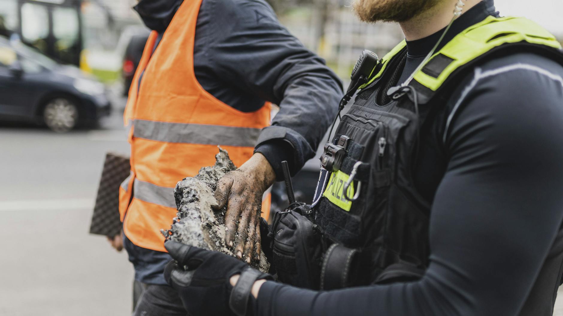 Ein Aktivist wird nach einer Klebe-Aktion am Ernst-Reuter-Platz mit Asphalt an der Hand abgeführt.