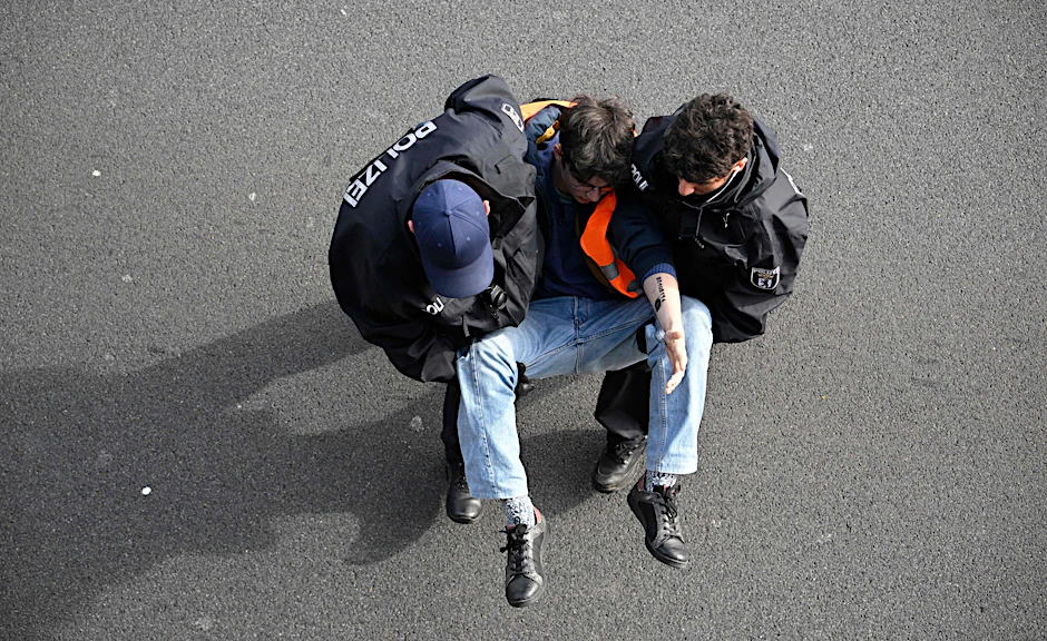 Ein Klimaaktivist der Letzten Generation wird von Polizisten weggetragen. Bei einigen Protesten der Gruppe soll es auch zu Sabotage-Aktionen auf Firmengeländen gekommen sein.