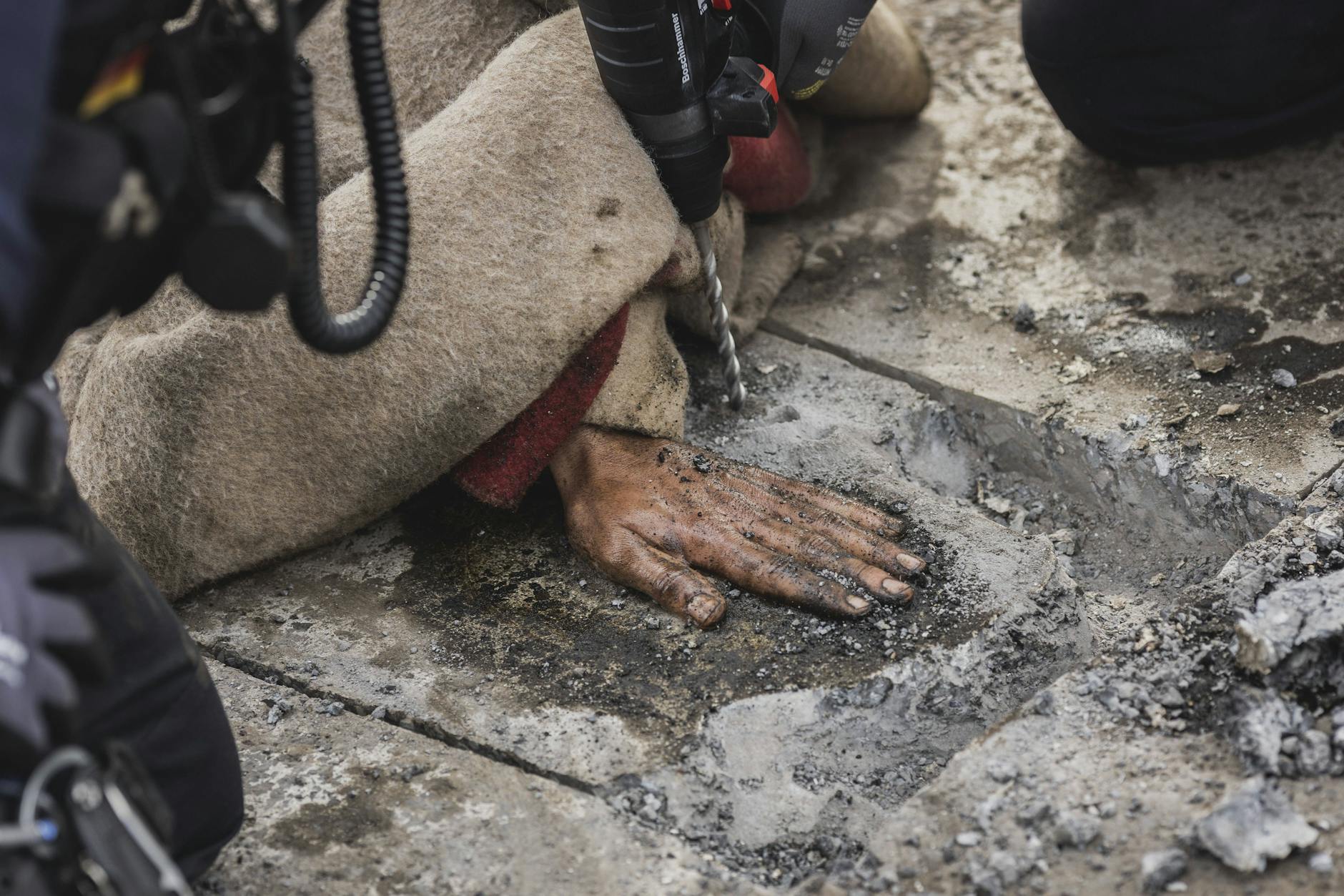 Die Hand eines Aktivisten wird mit einer Schlagbohrmaschine nach einer Klebeaktion am Ernst-Reuter-Platz von der Straße entfernt.
