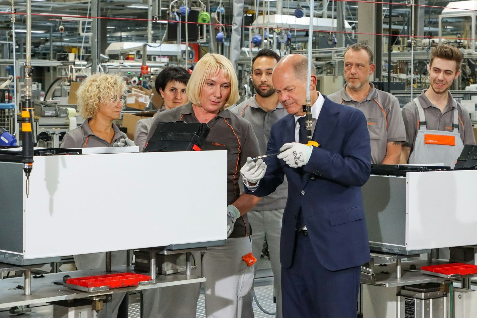 Bundeskanzler Olaf Scholz (SPD) schraubt unter Anleitung einer Viessmann-Mitarbeiterin die letzte Schraube in eine Wärmepumpe.
