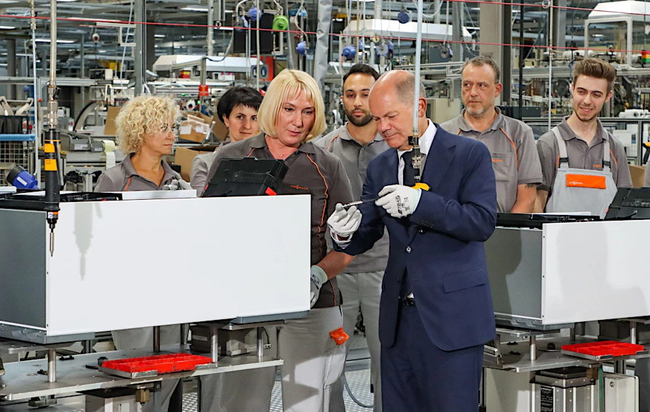 Bundeskanzler Olaf Scholz (SPD) schraubt unter Anleitung einer Viessmann-Mitarbeiterin die letzte Schraube in eine Wärmepumpe.