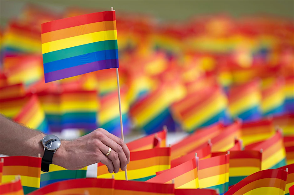 Ein Mann hält ein Regenbogenfähnchen in der Hand.  d