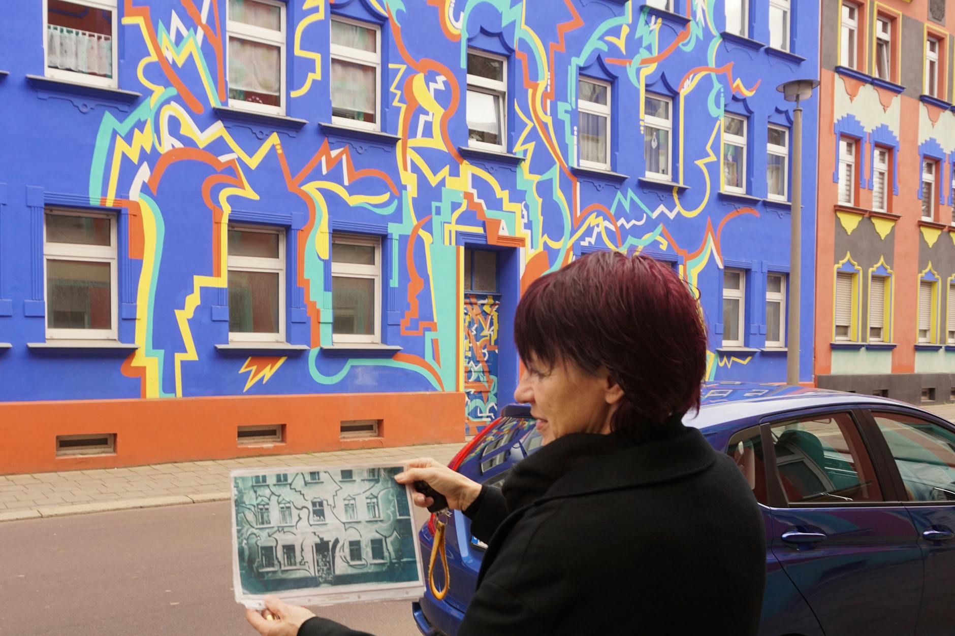 Die von Carl Krayl entworfene Fassade in der Otto-Richter-Straße wurde wieder hergestellt, wie Carmen Niebergall an einem alten Foto zeigt. Auch die Fassaden der Nachbarhäuser sind knallbunt.