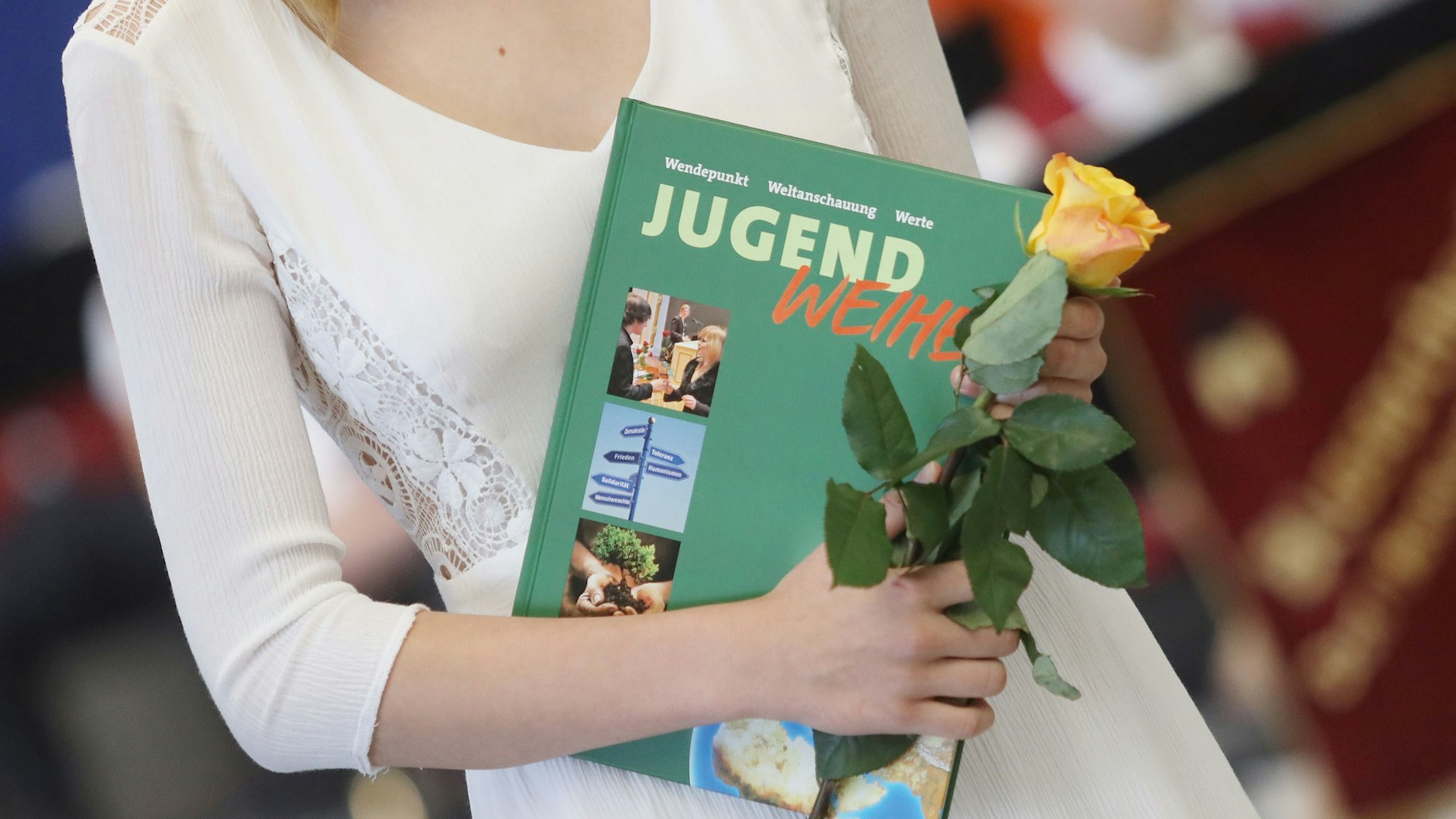 Eine Teilnehmerin der Jugendweihefeier steht mit einer Rose und einem Buch in der Hand in der Sport- und Mehrzweckhalle Dorf Mecklenburg. Die vor allem in Ostdeutschland populären Feiern am Übergang vom Kindes- in das Jugendalter finden üblicherweise im Frühjahr statt.