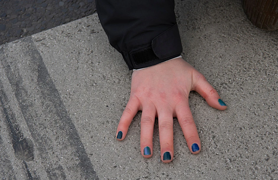 Mit bunten Fingernägeln sitzt eine Aktivistin  bei einer Blockade der Gruppierung Letzte Generation.  