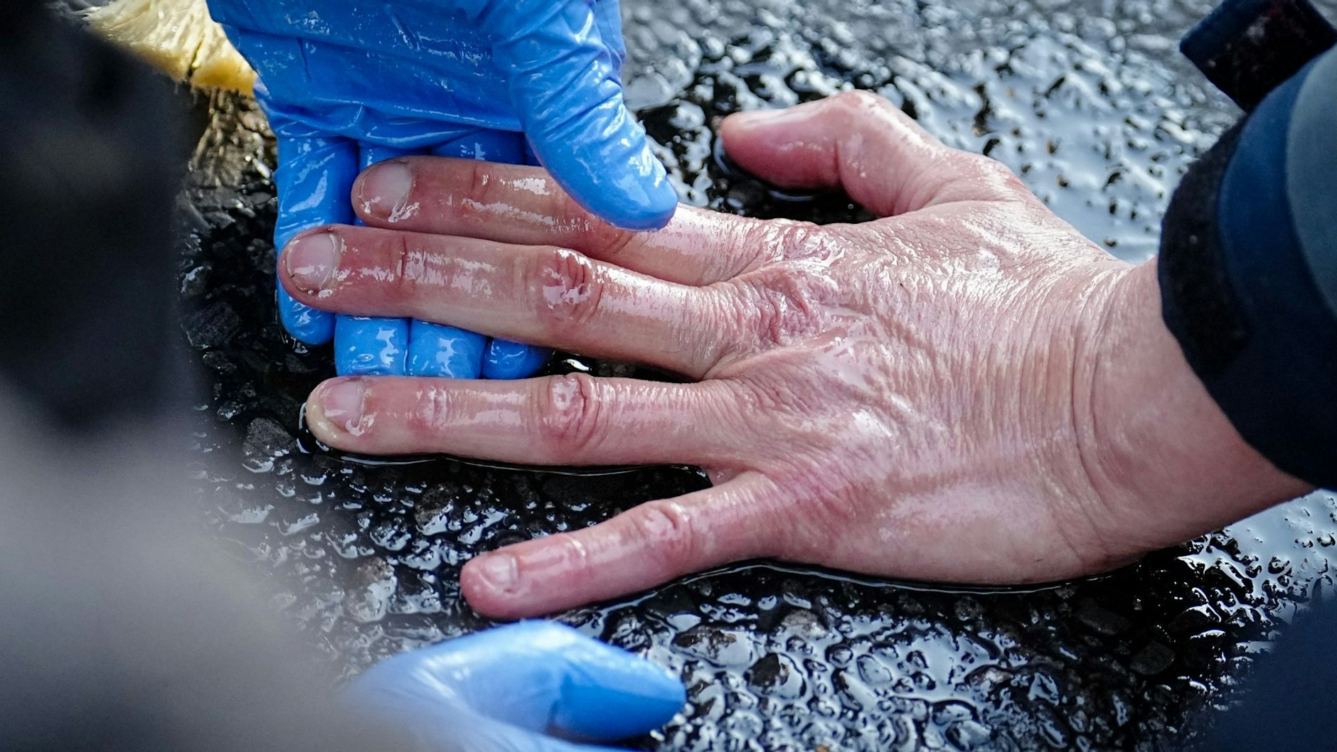 Ein Polizeibeamter löst die Hand eines Klimaaktivisten von der Straße. 