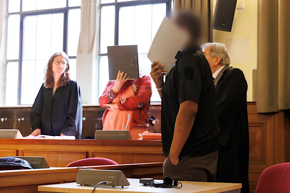 Die beiden Angeklagten verdecken im Gerichtssaal vor Sitzungsbeginn in Tübingen ihre Gesichter.  
