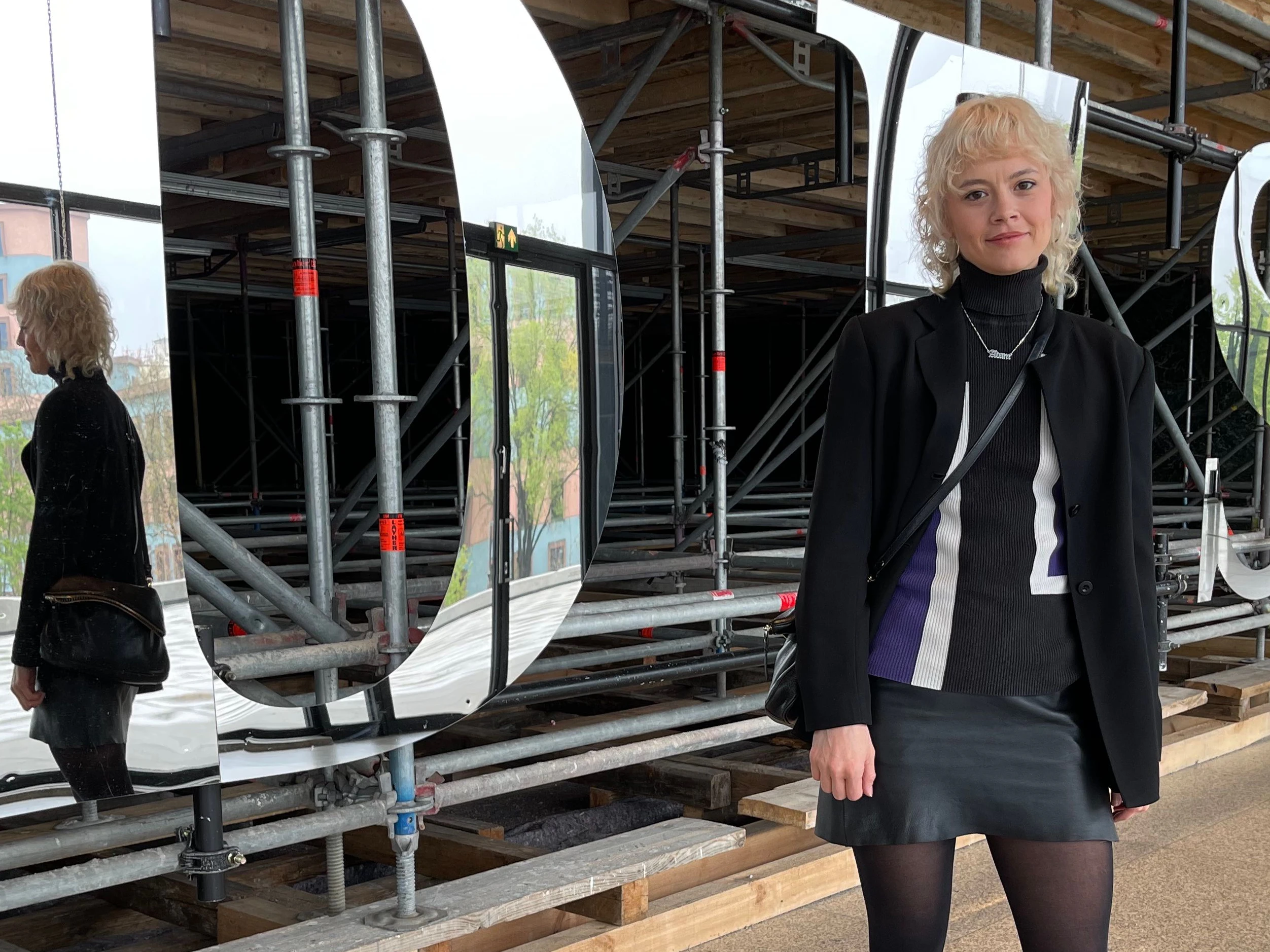 Brighid arbeitet in der Galerie Tanja Wagner. Ihr wasserstoffblond-gelockter Wolf Cut ist geradezu engelhaft. Hinter ihr ist ein Teil der fantasievollen Installation zu sehen, die Monica Bonvicini in der Neuen Nationalgalerie errichtet hat.
