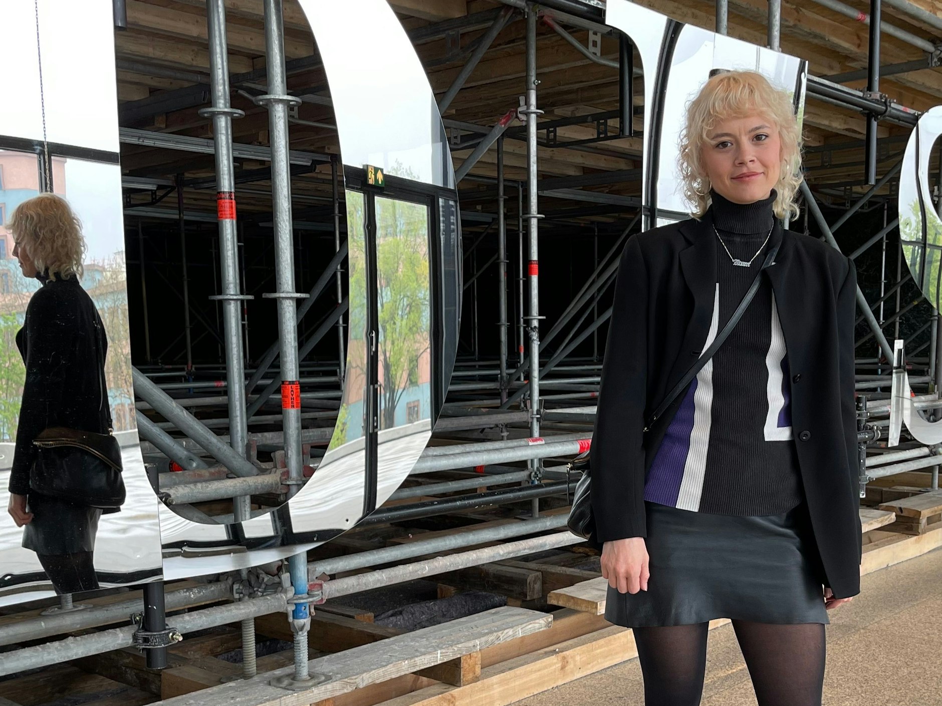 Brighid arbeitet in der Galerie Tanja Wagner. Ihr wasserstoffblond-gelockter Wolf Cut ist geradezu engelhaft. Hinter ihr ist ein Teil der fantasievollen Installation zu sehen, die Monica Bonvicini in der Neuen Nationalgalerie errichtet hat.