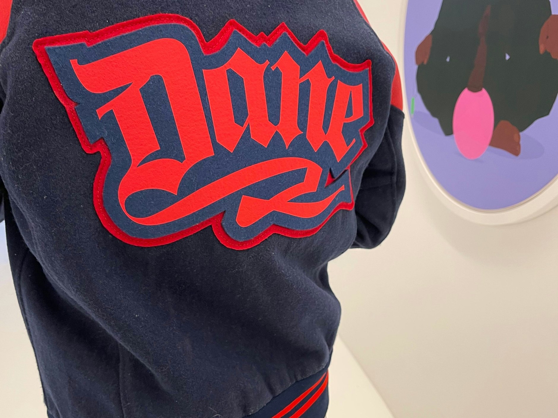 Auch dieser Rücken bietet etwas an. Andrés Collegejacke ist mit dem Schriftzug „Dane“ versehen. Das war sein Pseudonym in der West-Berliner Sprayer-Szene der 80er-Jahre. An der Wand: Kunst von Dennis Osadebe.