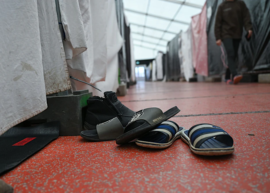 ARCHIV - Schuhe einer Flüchtlingsfamilie sind in einem Zelt der Flüchtlingsunterkunft vor einer Wohnparzelle abgestellt.  