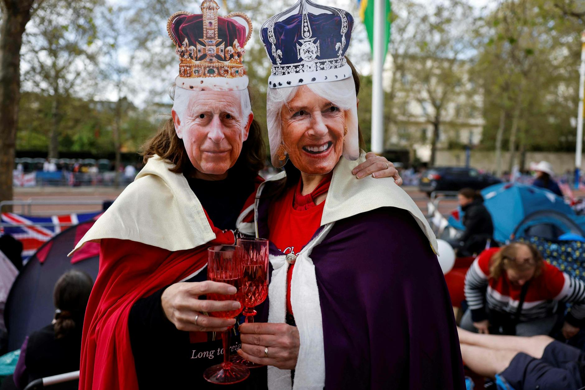 Partystimmung in London auf der Straße „The Mall“. Mit Masken von König Charles III (L) und Camilla, Queen Consort (R), zeigen die Wartenden den typisch britischen Humor.
