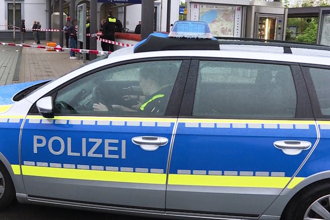 Polizisten sitzen in einem Polizeiauto vor dem abgesperrten Tatort am Bahnhof in Wunstorf.