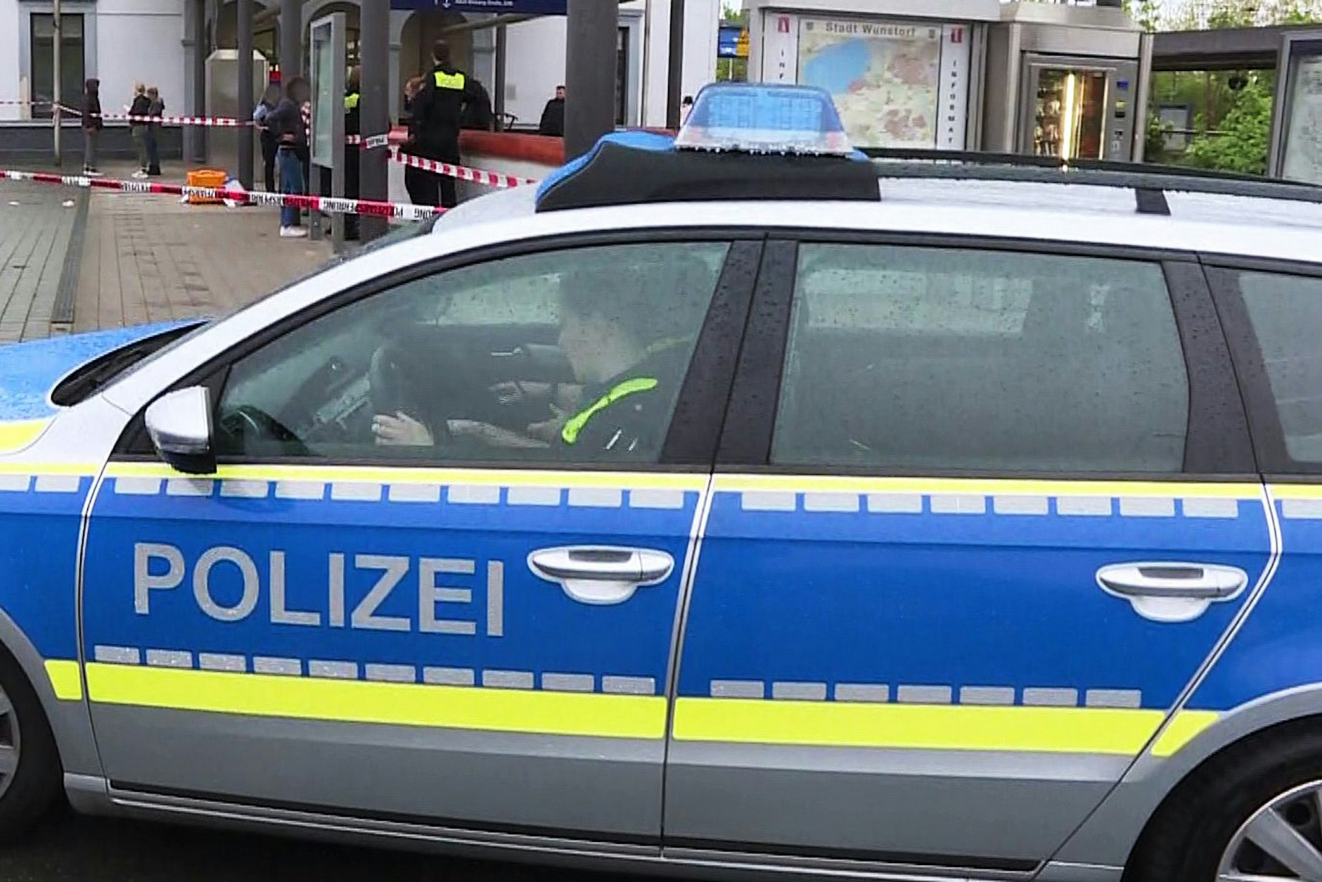Polizisten sitzen in einem Polizeiauto vor dem abgesperrten Tatort am Bahnhof in Wunstorf.