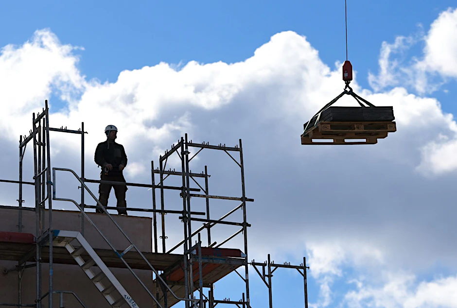ARCHIV - Ein Arbeiter dirigiert auf einer Baustelle einen Kran.  a