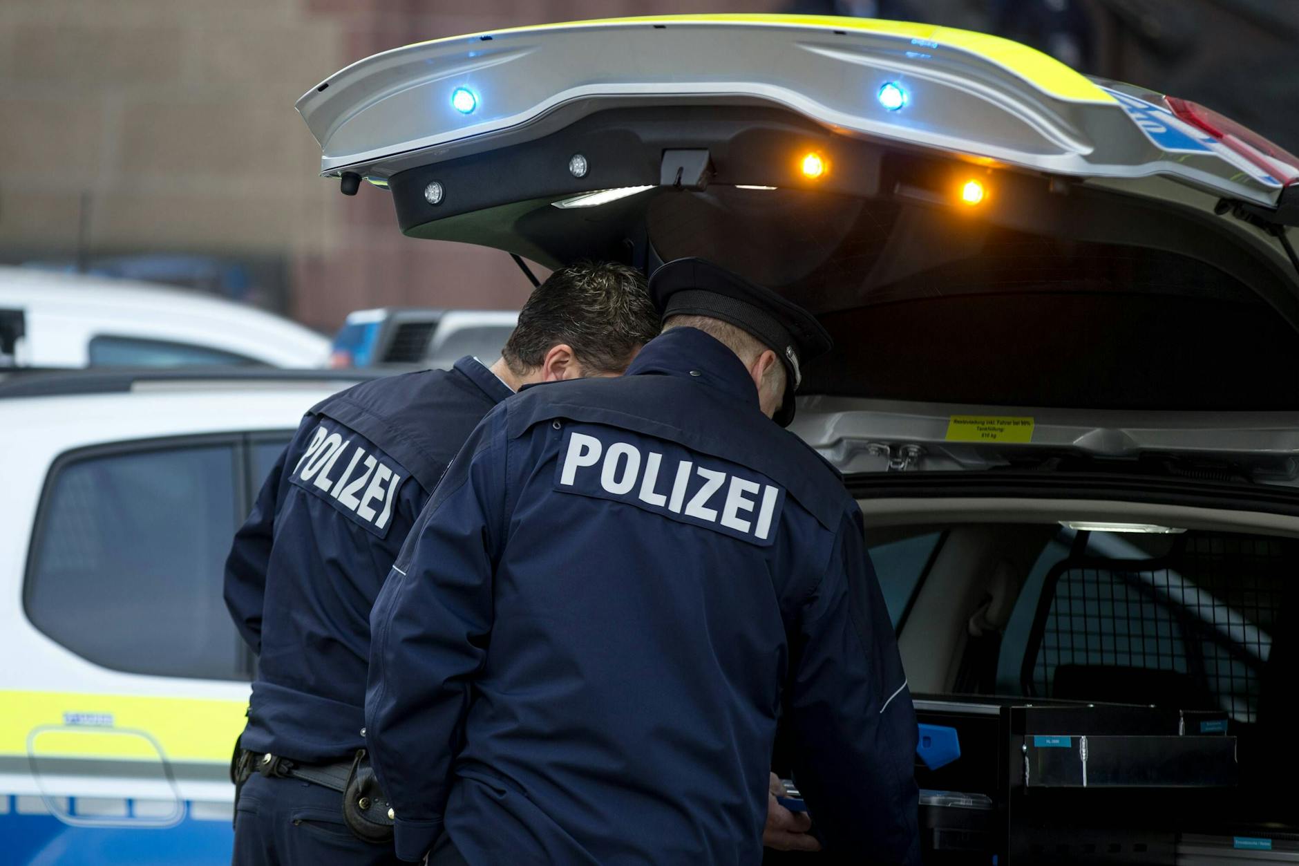 Zwei Polizisten stehen bei einem Einsatz am Streifenwagen (Symbolbild). 