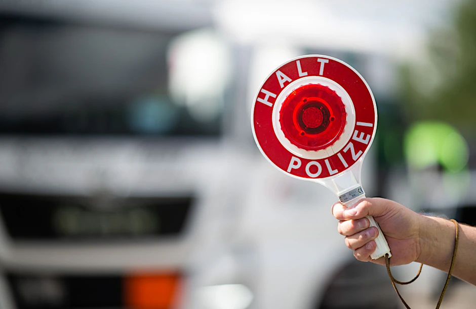 Ein Polizist hält bei einer Verkehrskontrolle eine Polizeikelle in der Hand.  