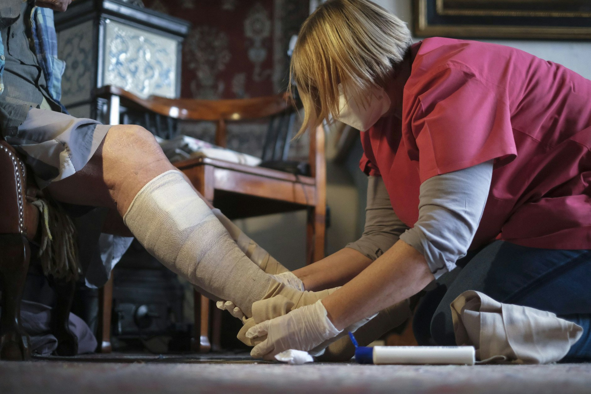Eine Pflegekraft verbindet das Bein einer Patientin in deren Wohnung.