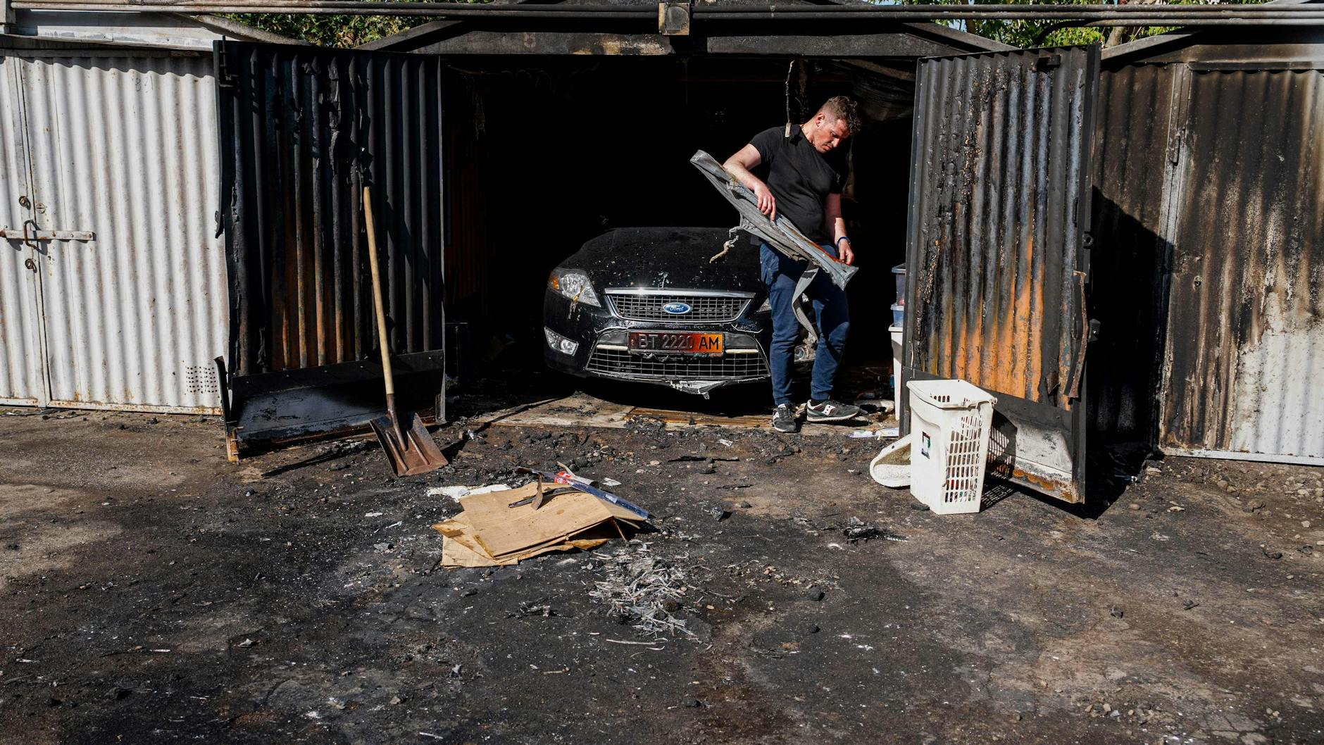 Ein Mann räumt auf: Trümmer einer über Kiew abgeschossenen Rakete entzündeten Feuer, sein Auto ist beschädigt.
