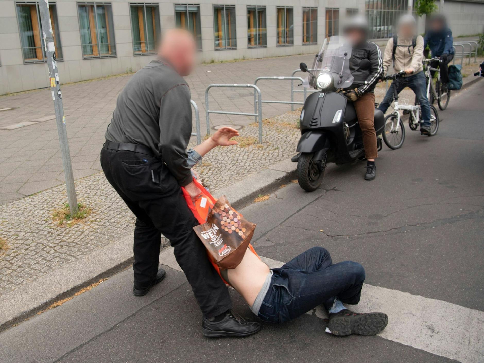 Bei einer Straßenblockade der Letzten Generation zieht ein Passant einen Aktivisten von der Straße.