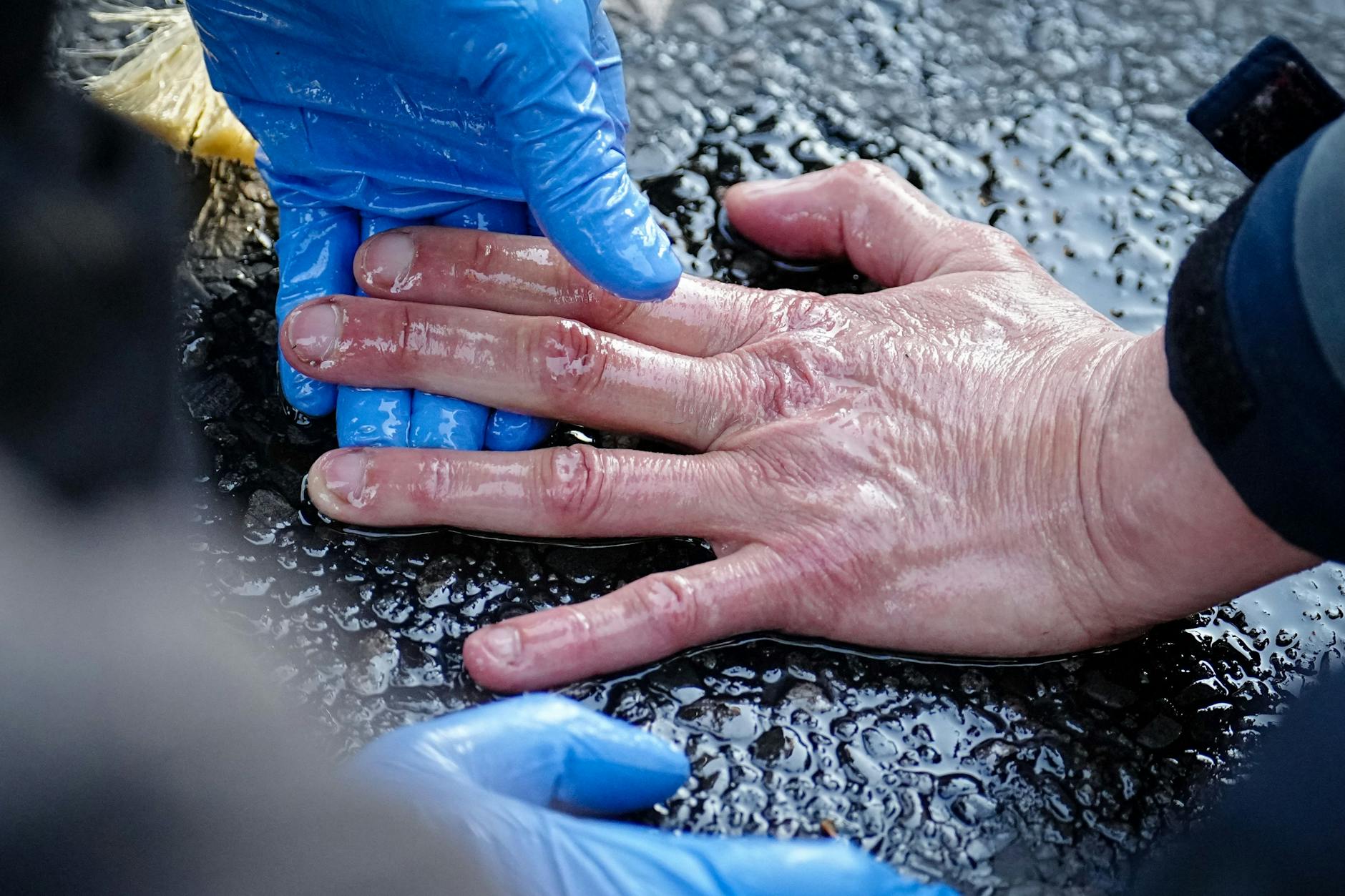 Die Hand eines Klima-Klebers wird vom Straßenasphalt gelöst.