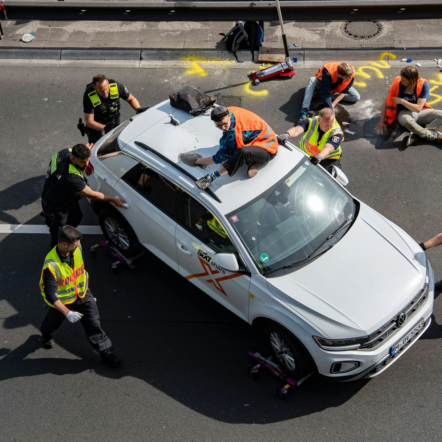 Polizisten schieben einen Wagen bei einer Blockade der Letzten Generation auf der Autobahn 100 auf den Standstreifen.
