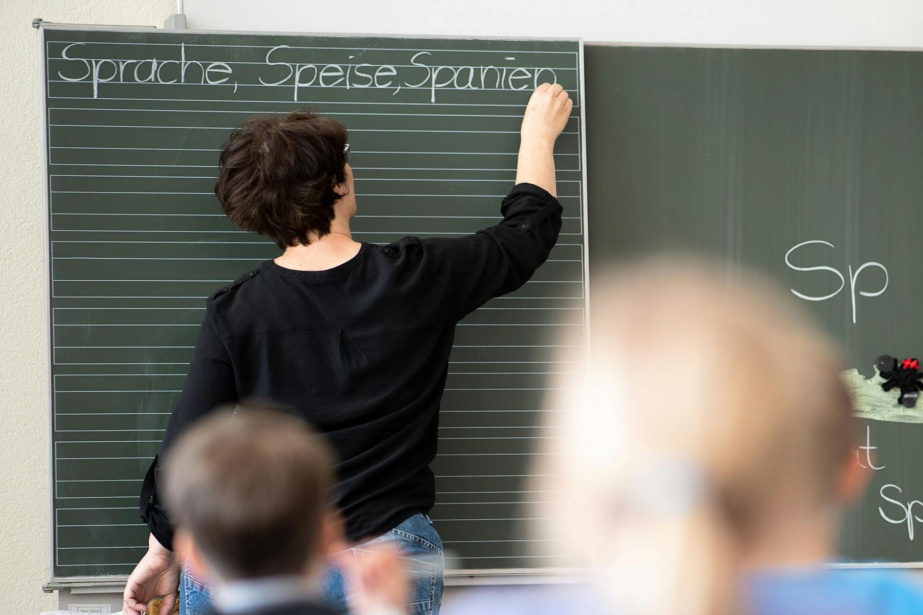 Eine Lehrerin steht an der Tafel in einer Klasse: Immer weniger Pädagogen unterrichten immer mehr Schüler in Berlin.