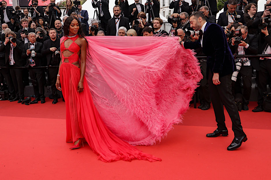 Naomi Campbell erfrischt anlässlich der 76. Fimfestspiele in Cannes mit Colorblocking auf dem roten Teppich. Die Cut-out-Couture von Valentino wird durch eine federbesetzte Schleppe in Pink ergänzt – die Campbells Begleiter, der Filmproduzenten Mohammed Al Turki, hier netterweise für die Fotos hübsch zurechtlegt.