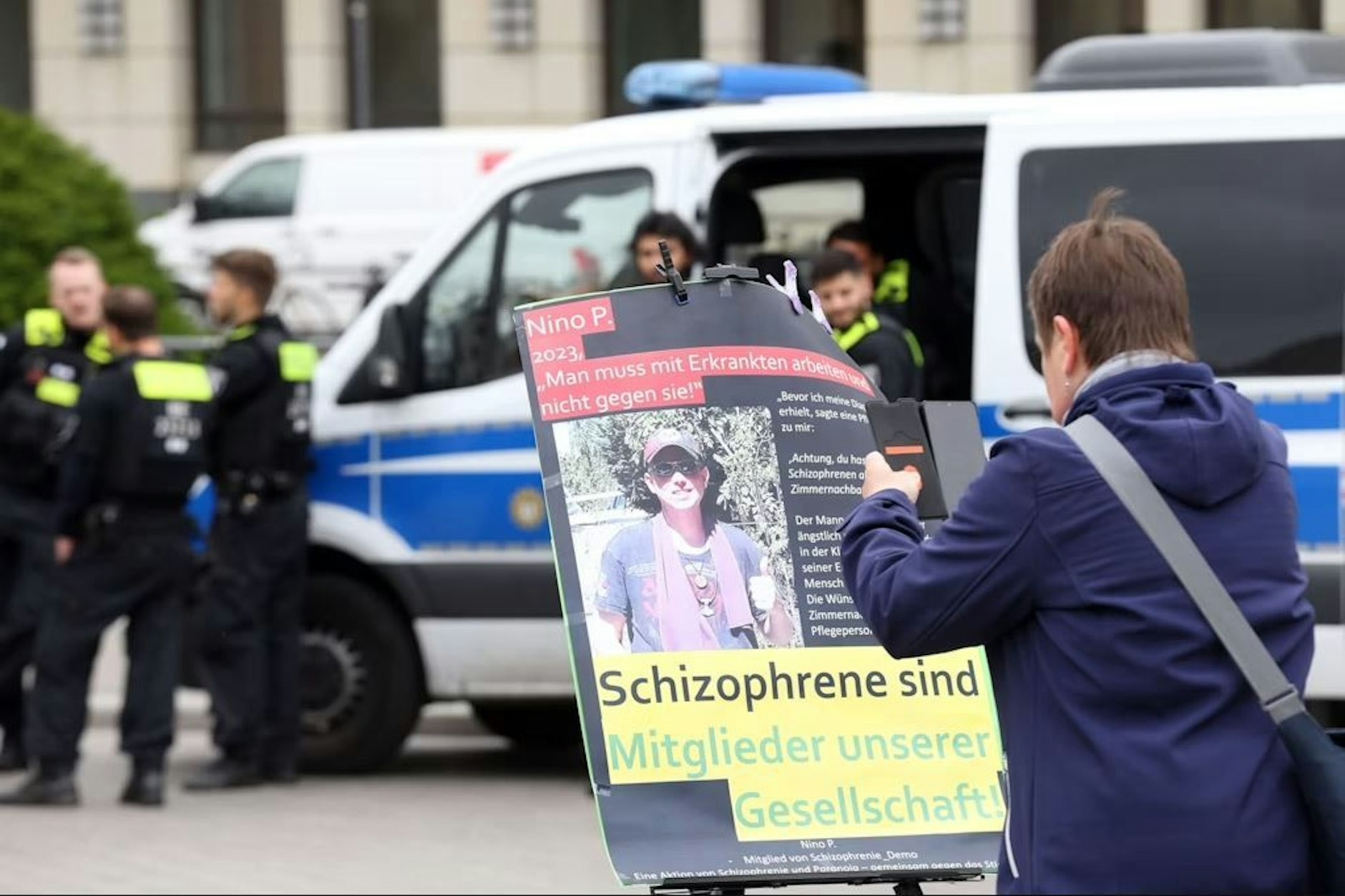 Eine Frau fotografiert ein Plakat auf einer Demo in Berlin zum Welt-Schizophrenie-Tag.