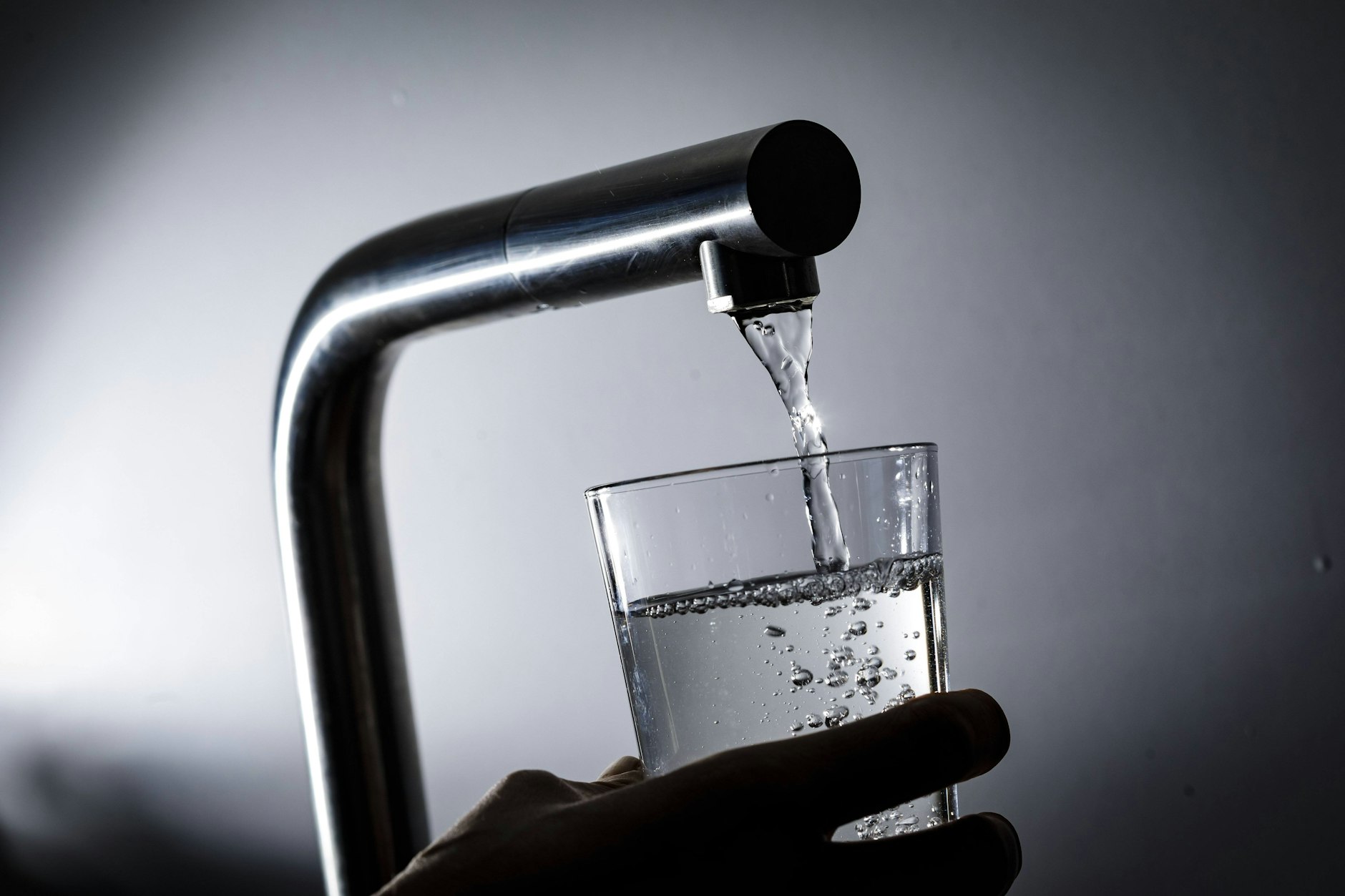 Wasser fließt aus einem Wasserhahn in ein Glas.&nbsp;