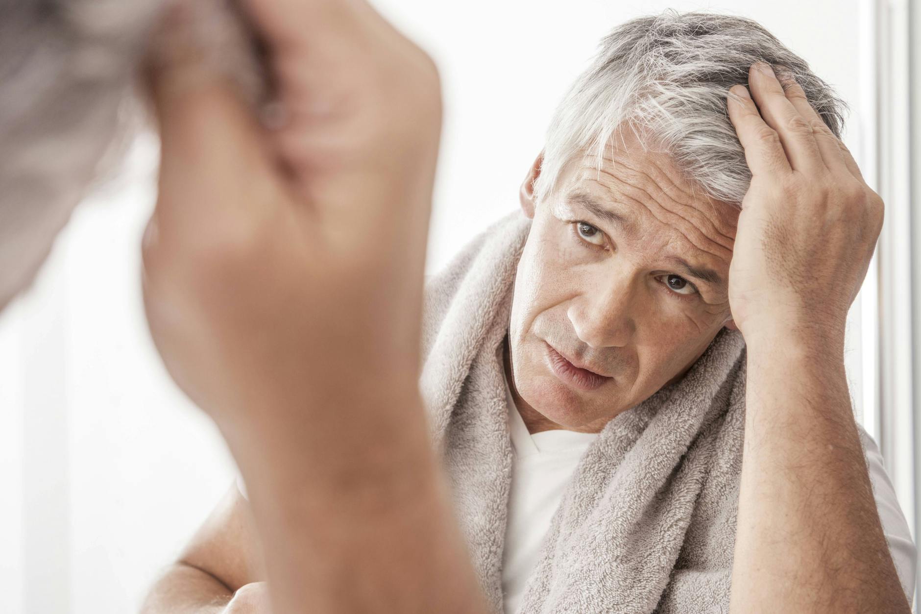 Es muss ja nicht so bleiben: Ein Mann fährt sich vorm Spiegel durchs graue Haar.