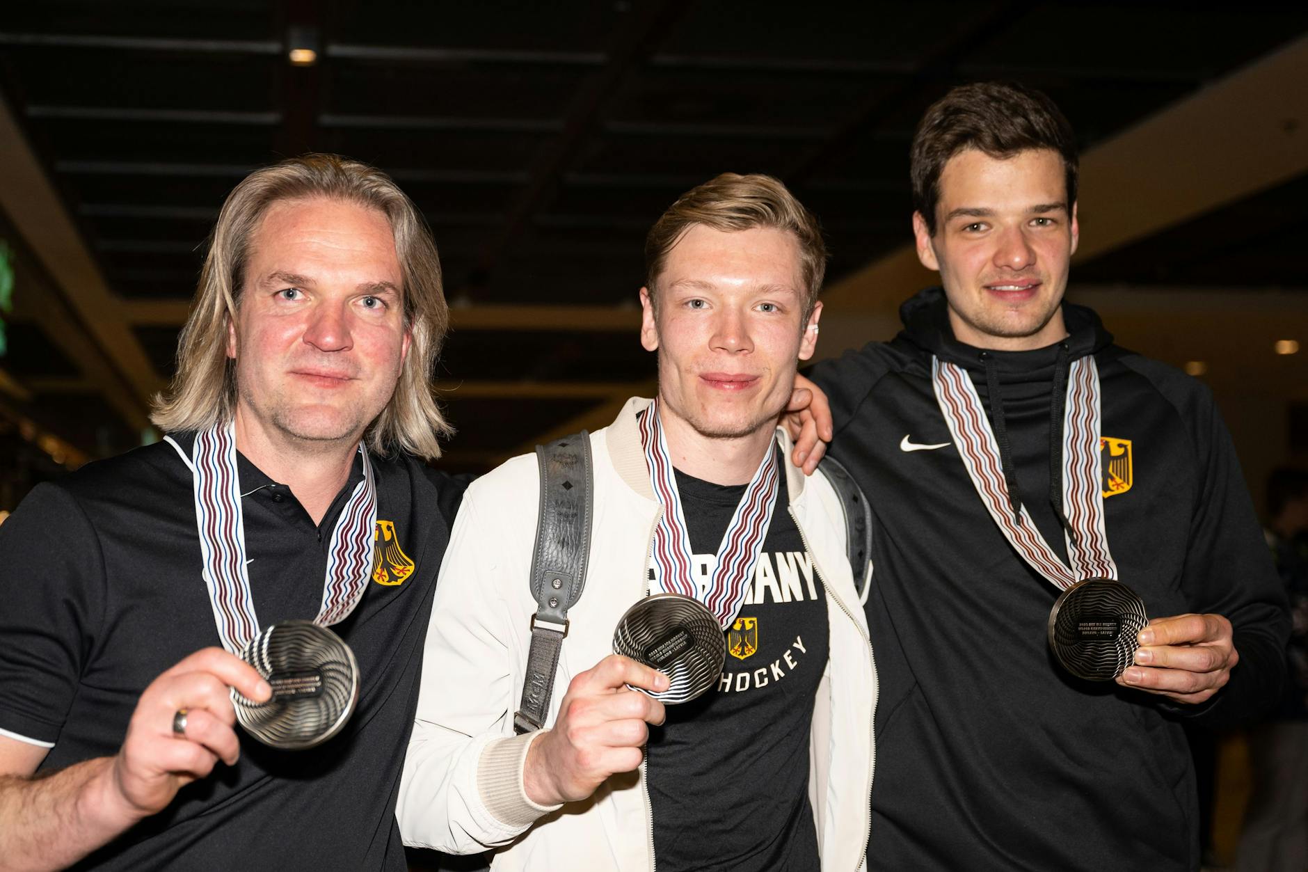 Nach der Rückkehr präsentieren Torwarttrainer Sebastian Elwing, Jonas Müller und Kai Wissmann (v.l.) am BER ihre WM-Silbermedaillen.