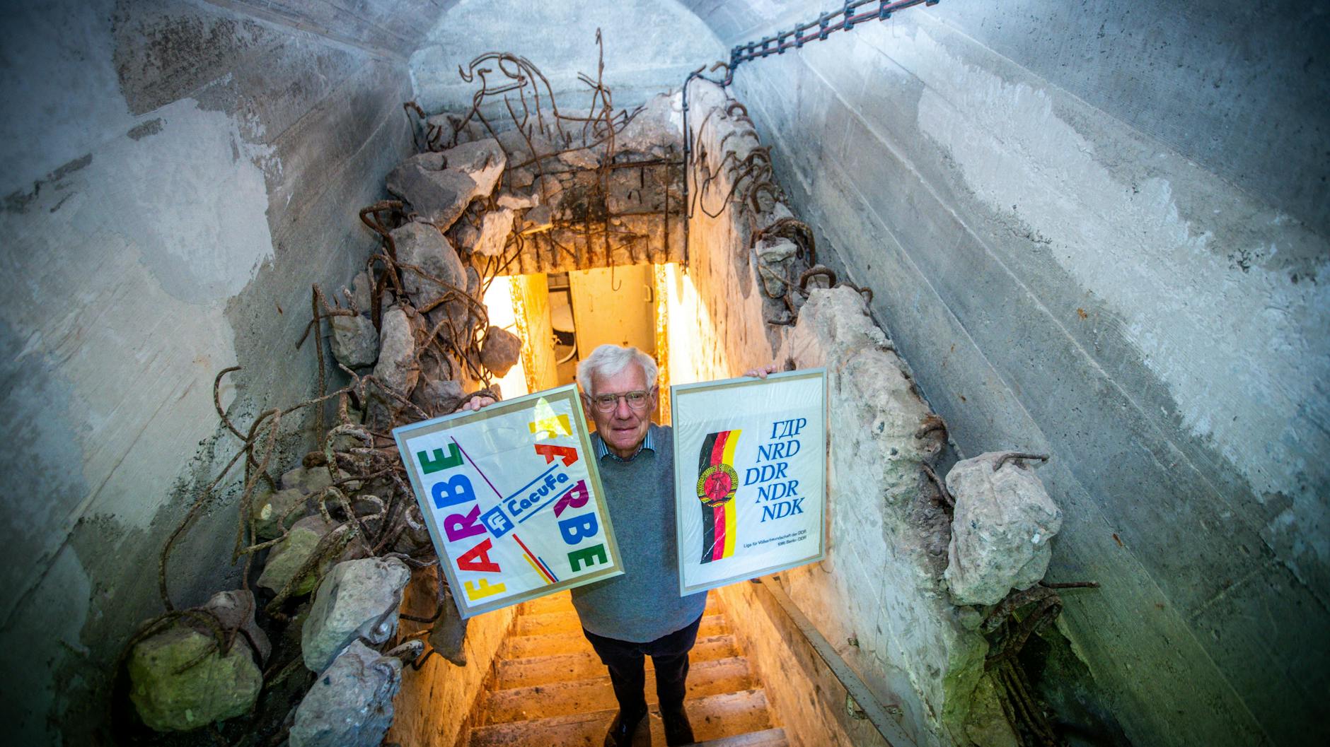 Dieter Luchs im Eingang zu dem ehemaligen DDR-Bunker, wo seine Plastiktüten-Ausstellung zu sehen ist. Er zeigt zwei Bilderrahmen mit Kunststofftaschen der Liga für Völkerfreundschaft der DDR (r.) und der Farbenfirma LacuFa. 