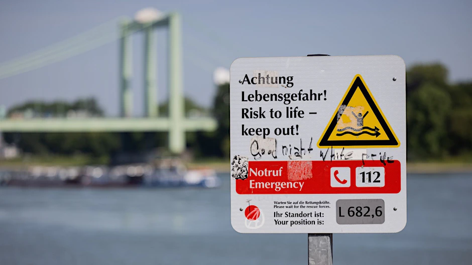 Ein Schild am Rheinufer weist auf die Gefahren beim Schwimmen im Fluss hin.  