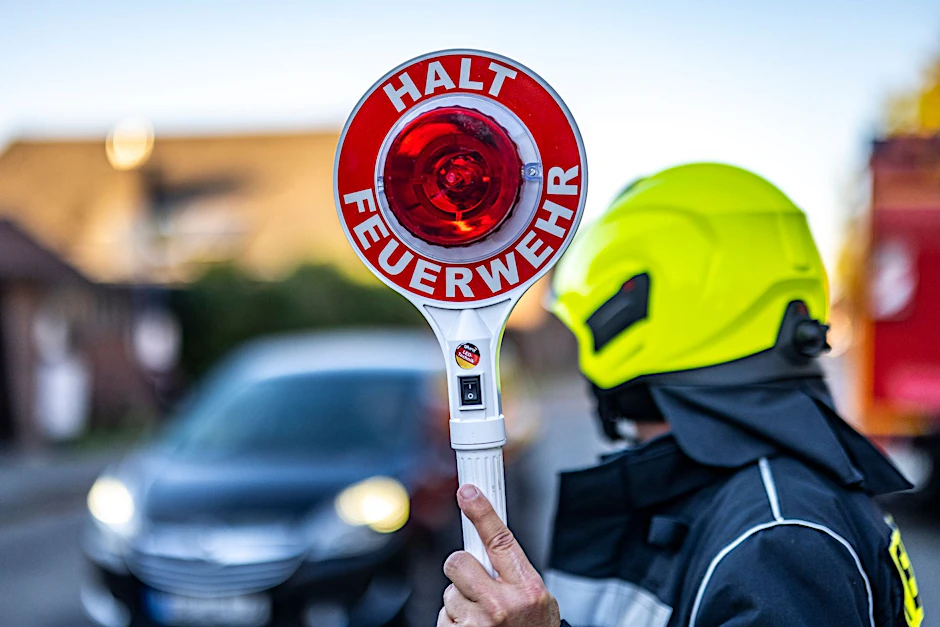 Ein Mitglied der Feuerwehr hält eine Kelle mit der Aufschrift «Halt Feuerwehr» in die Höhe.  