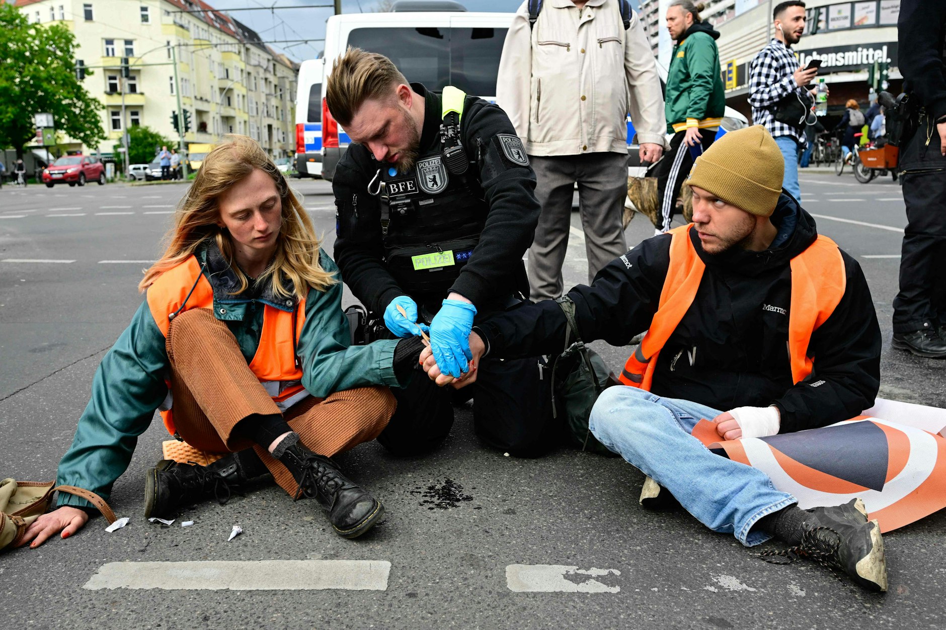 Ein Polizist versucht, Aktivisten der Letzten Generation in Berlin von der Straße zu lösen.