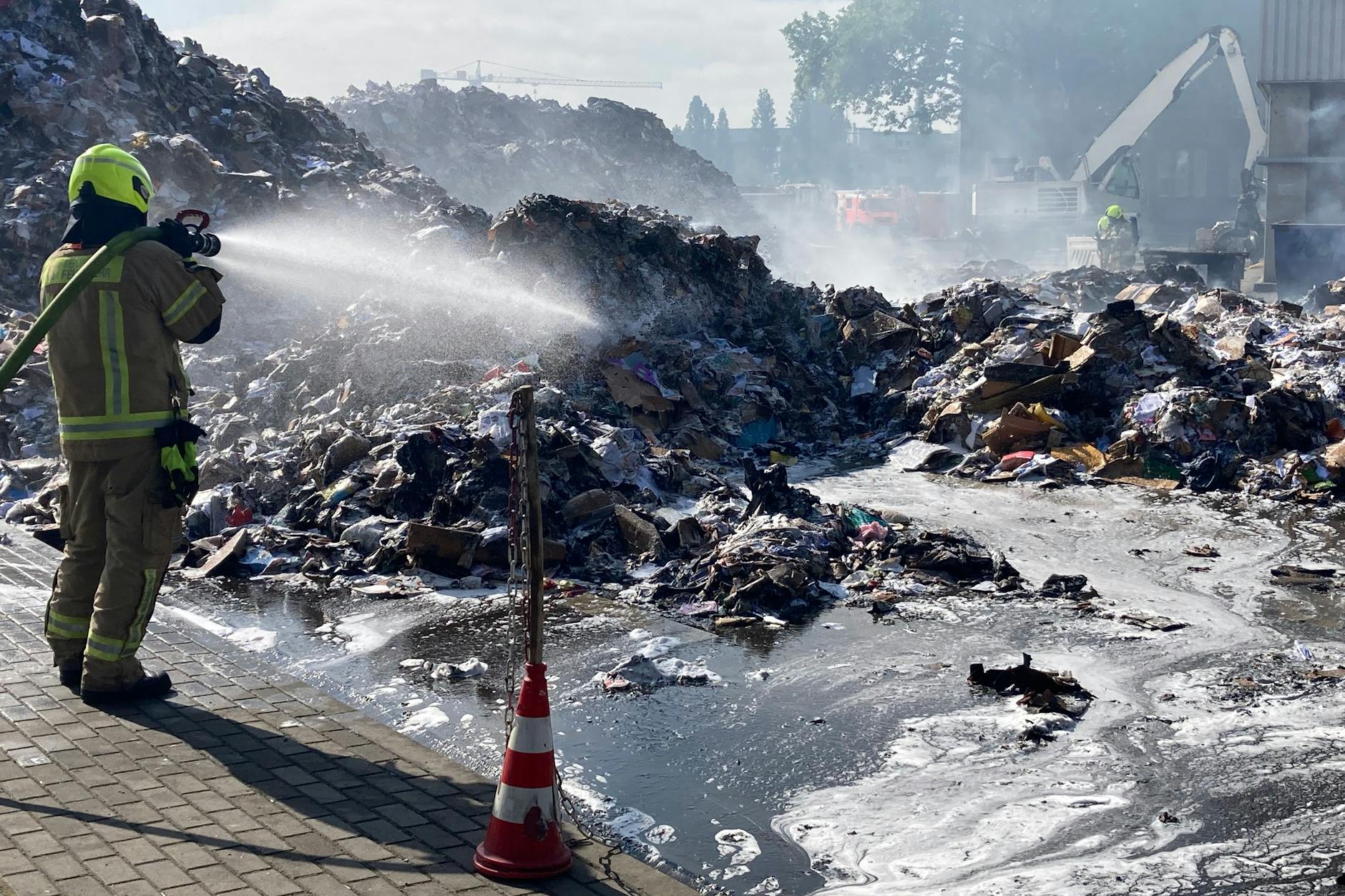 Remondis-Mitarbeiter fahren aktuell mit Bulldozern in die Halle, um das verbrannte Papier zu entfernen. Die Feuerwehr löscht anschließend die Papierhaufen.